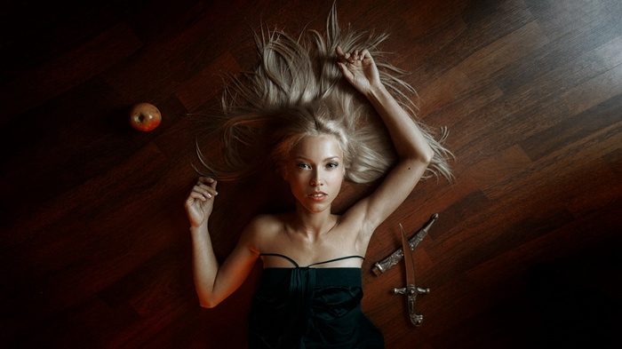 Woman with blonde hair lying on the floor with an apple and a dagger