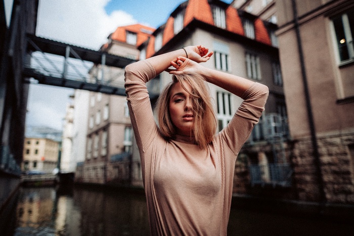 Woman with arms raised in front of buildings and canal