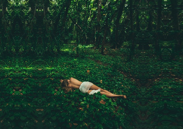 Woman lying in a green forest covered in leaves