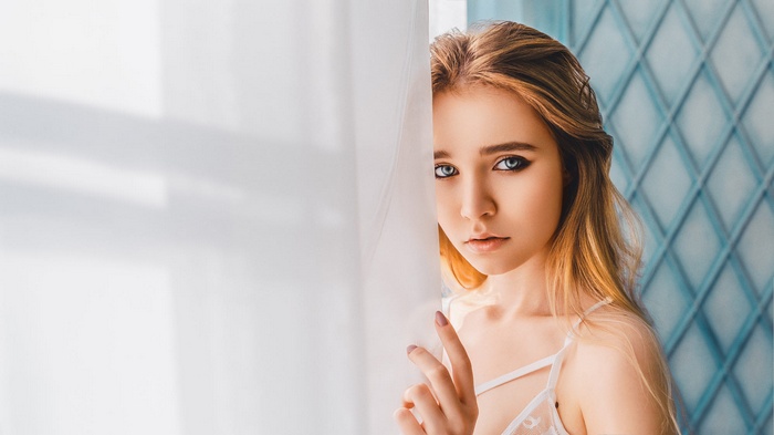 Woman with blue eyes peeking through curtains