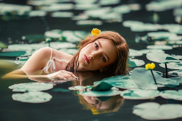 Woman with yellow flower in hair in pond with lily pads