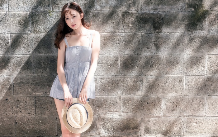Asian woman holding a straw hat in front of a brick wall