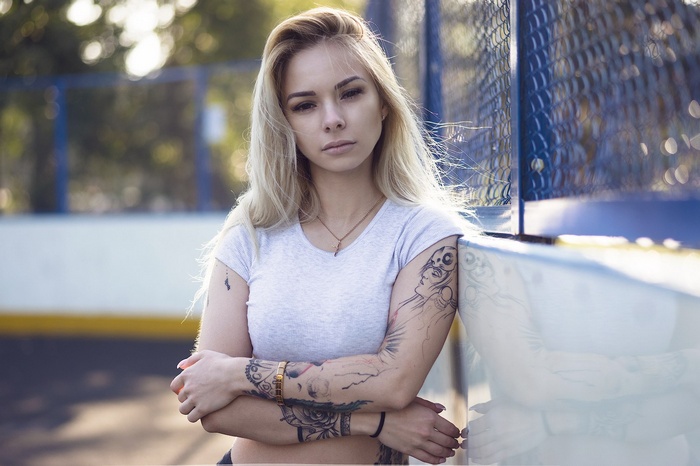 Woman with tattoos leaning against a fence