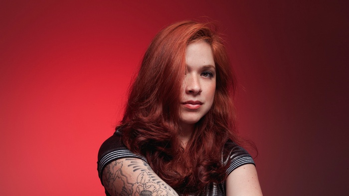 Woman with red hair and tattoos on red background