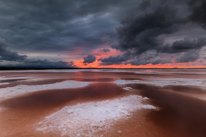 Dark clouds over a pink salt lake at sunset