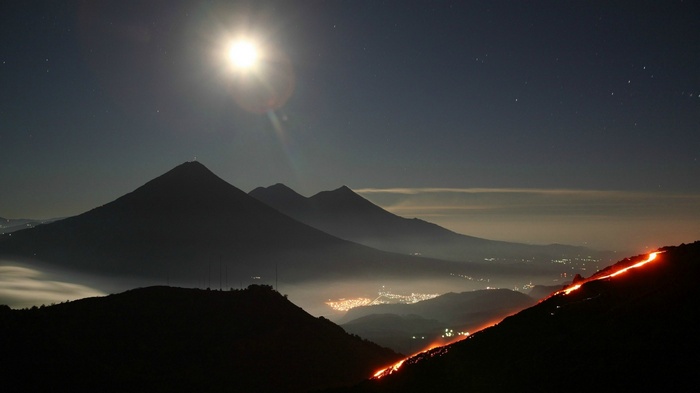 Volcano eruption at night with moon and city lights