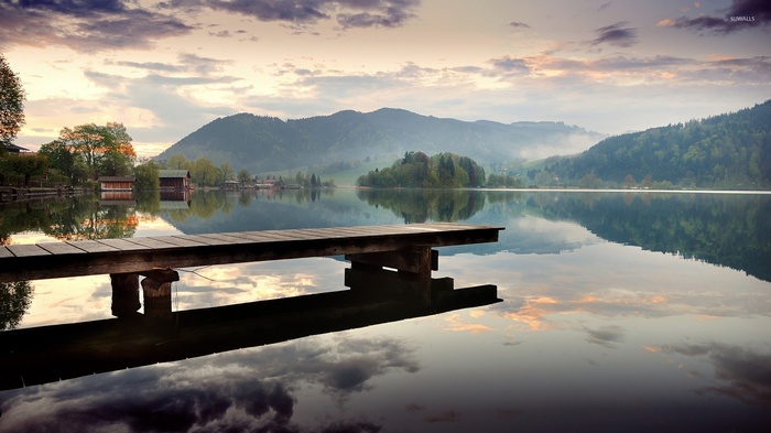 Wooden pier on a calm lake with misty mountains