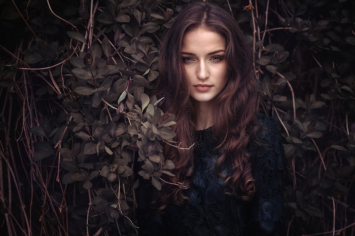 Woman with long brown hair in front of dark foliage