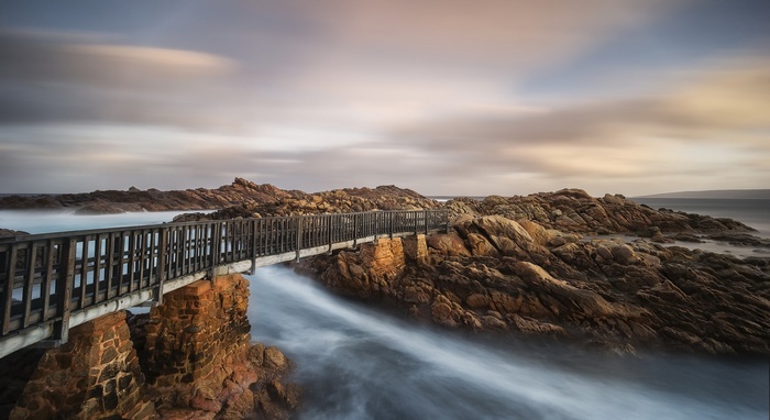 Wooden bridge over rocky coastline with flowing water