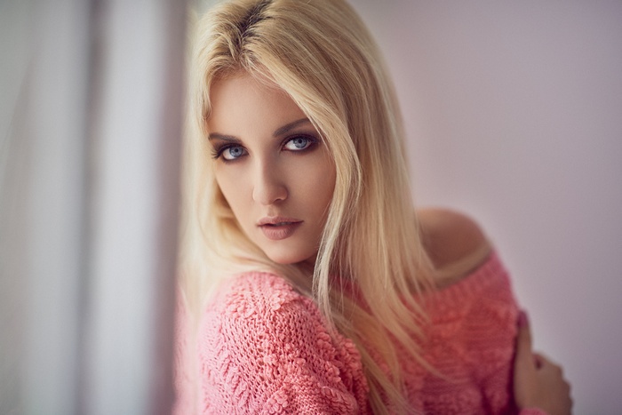 Blonde woman with blue eyes wearing a pink sweater