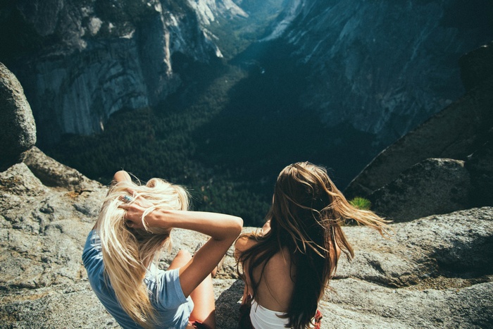 Two women sitting on a cliff overlooking a valley