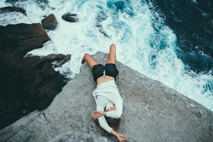 Woman lying on cliff edge overlooking ocean