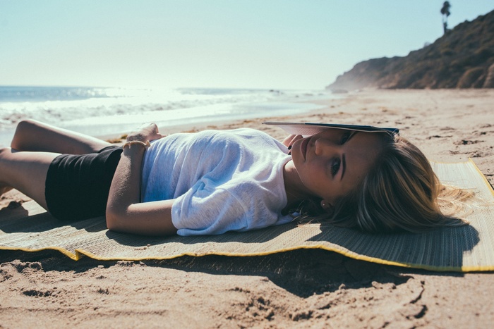 Woman lying on beach with book over face