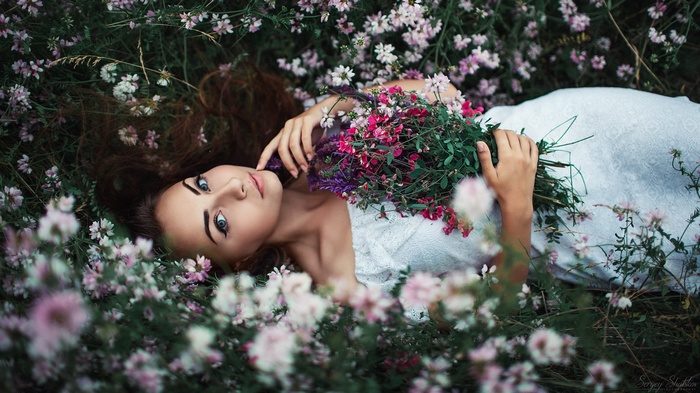 Woman lying in a field of flowers holding a bouquet