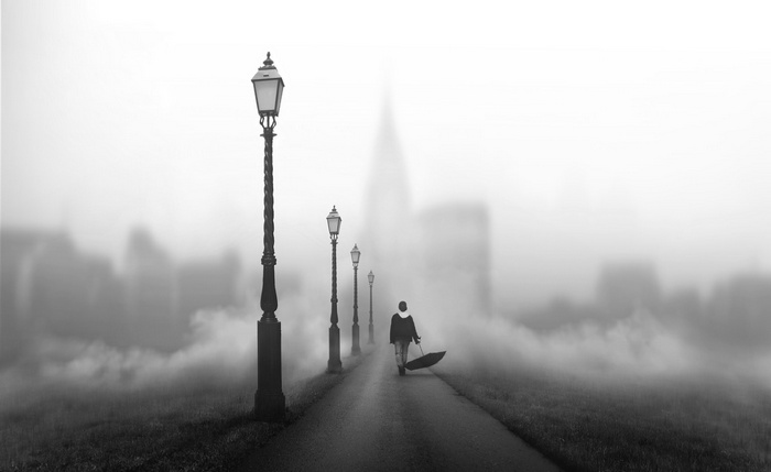 Man with umbrella walking on foggy street with lanterns