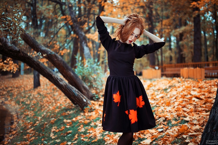 Woman with red hair in a black dress in autumn park