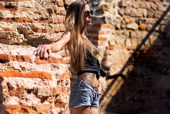 blonde, belly, tattoo, women, depth of field, skinny, jean shorts, sunglasses, looking away, long hair, bricks, T-shirt