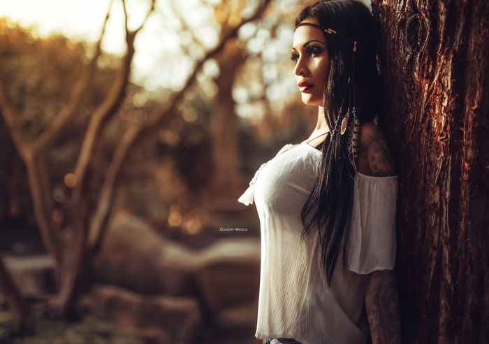 Woman with tattoos and hair beads leaning against a tree