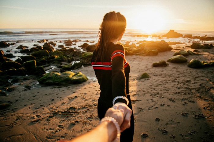 Woman holding hand on beach at sunset