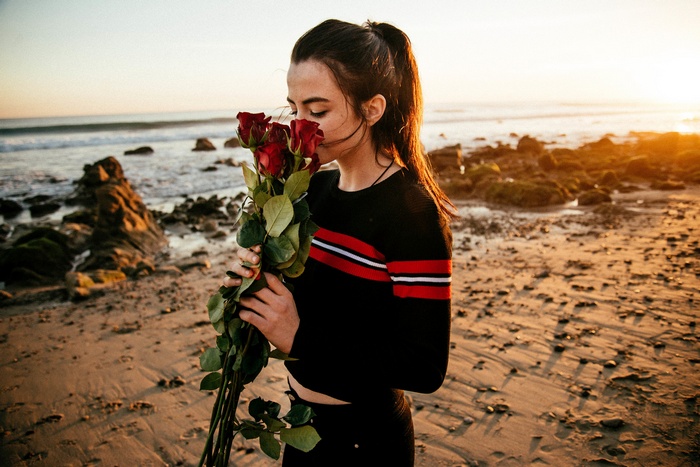 Woman smelling red roses on a beach at sunset