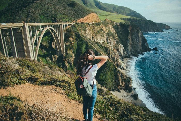 Woman with backpack on cliff overlooking ocean and bridge