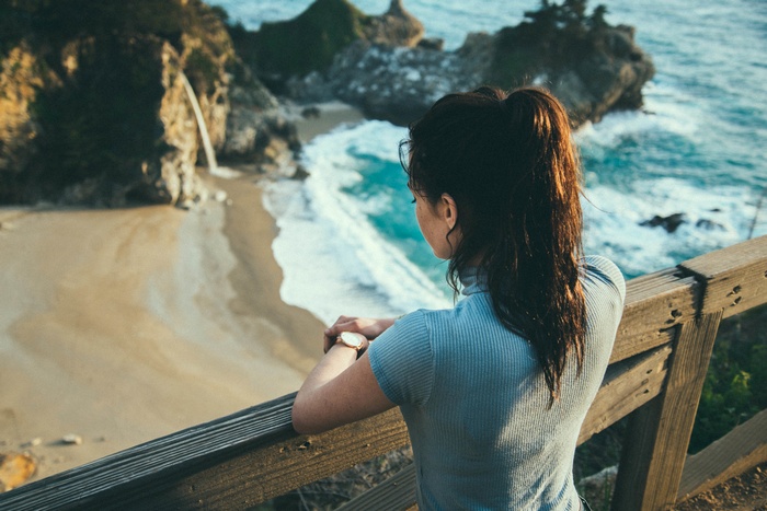 Woman looking at waterfall and ocean from a wooden railing