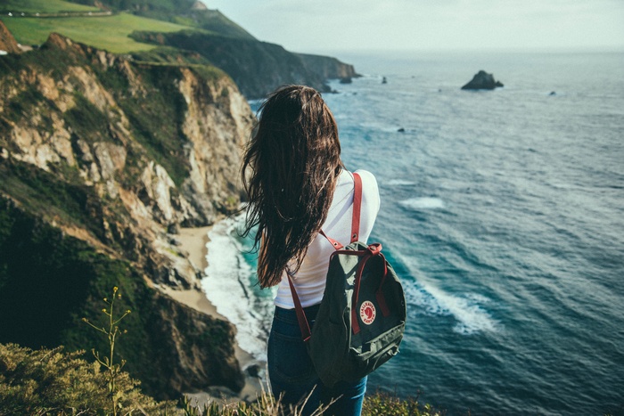 Woman with backpack overlooking the ocean and cliffs