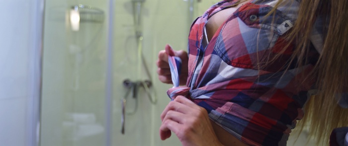 Woman tying a plaid shirt in a bathroom