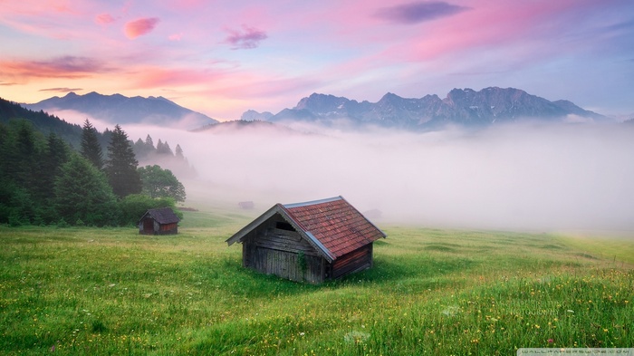 Wooden cabins in a misty mountain valley at sunrise