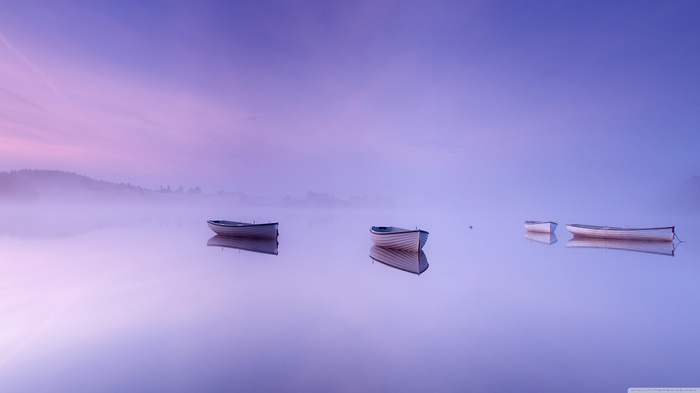 Three boats on a misty lake at sunrise