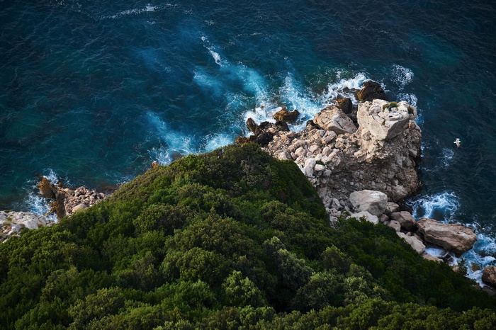 Overhead view of a green cliff overlooking a rocky coast and blue ocean