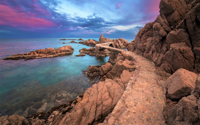 Rocky coast with stone path and bridge at sunset