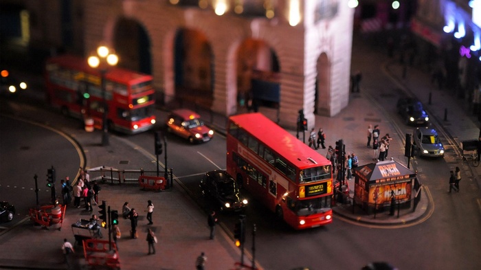 Tilt shift view of London double-decker buses and traffic at night