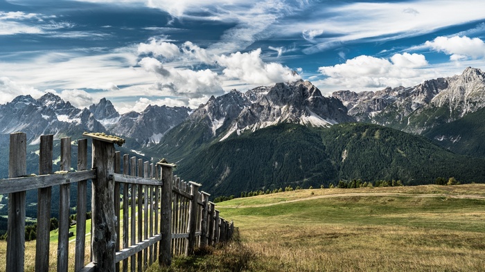 Wooden fence in front of mountains under a cloudy sky