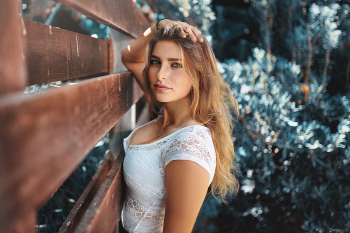 Woman with blonde hair leaning against a wooden fence