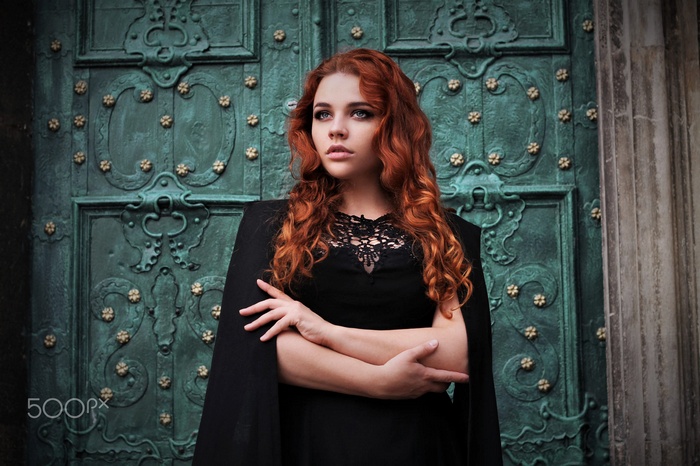 Woman with red wavy hair in black dress in front of ornate door