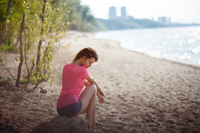Woman in pink shirt sitting on a rock on the beach