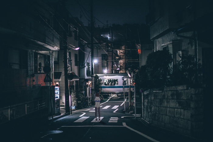 Girl on a street at night with a train passing