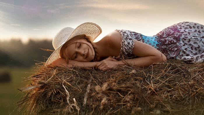 Woman in hat sleeping on hay bale