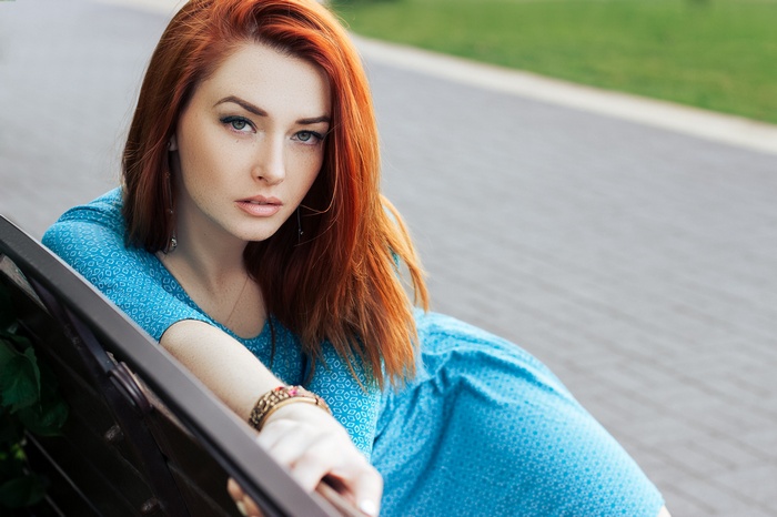 Woman with red hair wearing a blue dress sitting on a bench