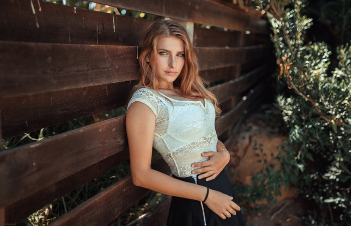 Woman in white lace top leaning on wooden fence
