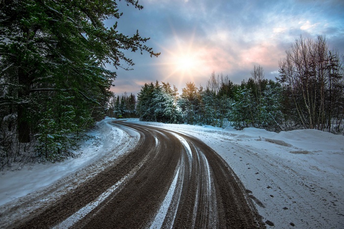 Winding winter road through a snowy forest with sun