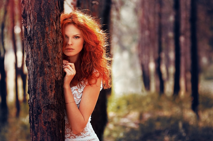 Redhead woman in white dress behind a tree