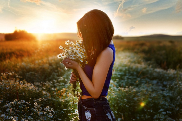 Woman holding daisies in a field at sunset