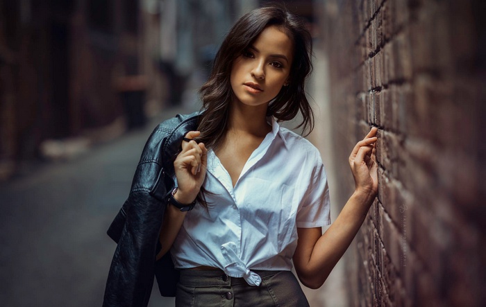 Woman in white shirt and leather jacket leaning on brick wall