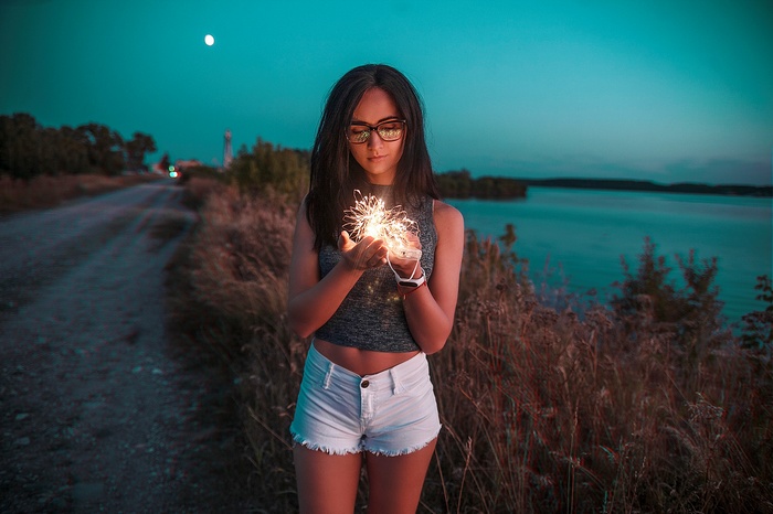 Woman holding sparklers by a lake at dusk