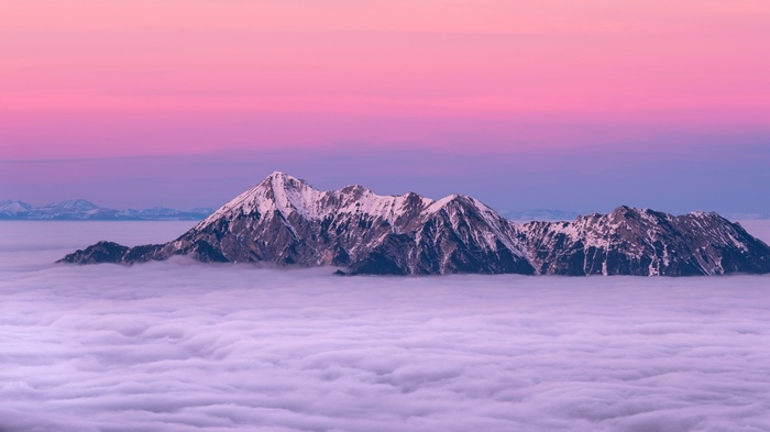 Snowy mountain range above clouds at sunset