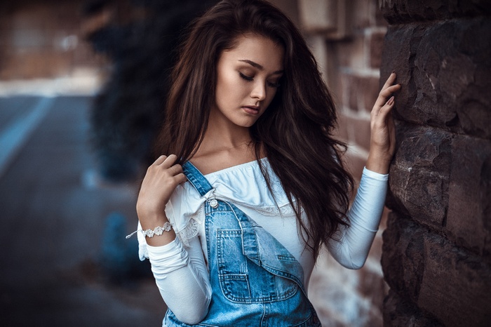 Woman in denim overalls leaning against a stone wall
