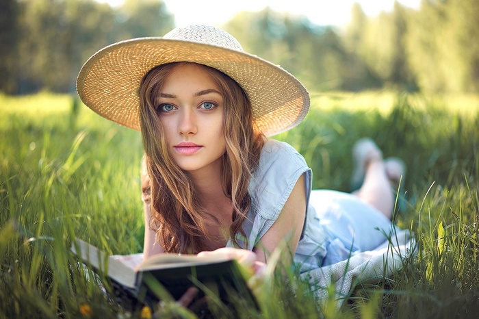 Woman in a straw hat reading a book in a grassy field
