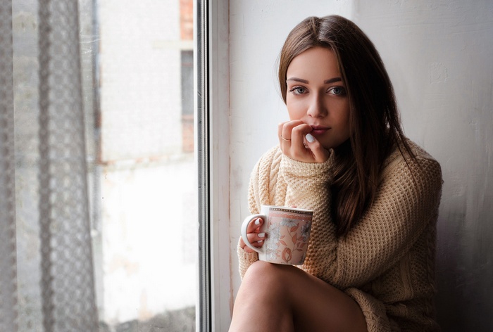 Woman with blue eyes holding a cup by the window